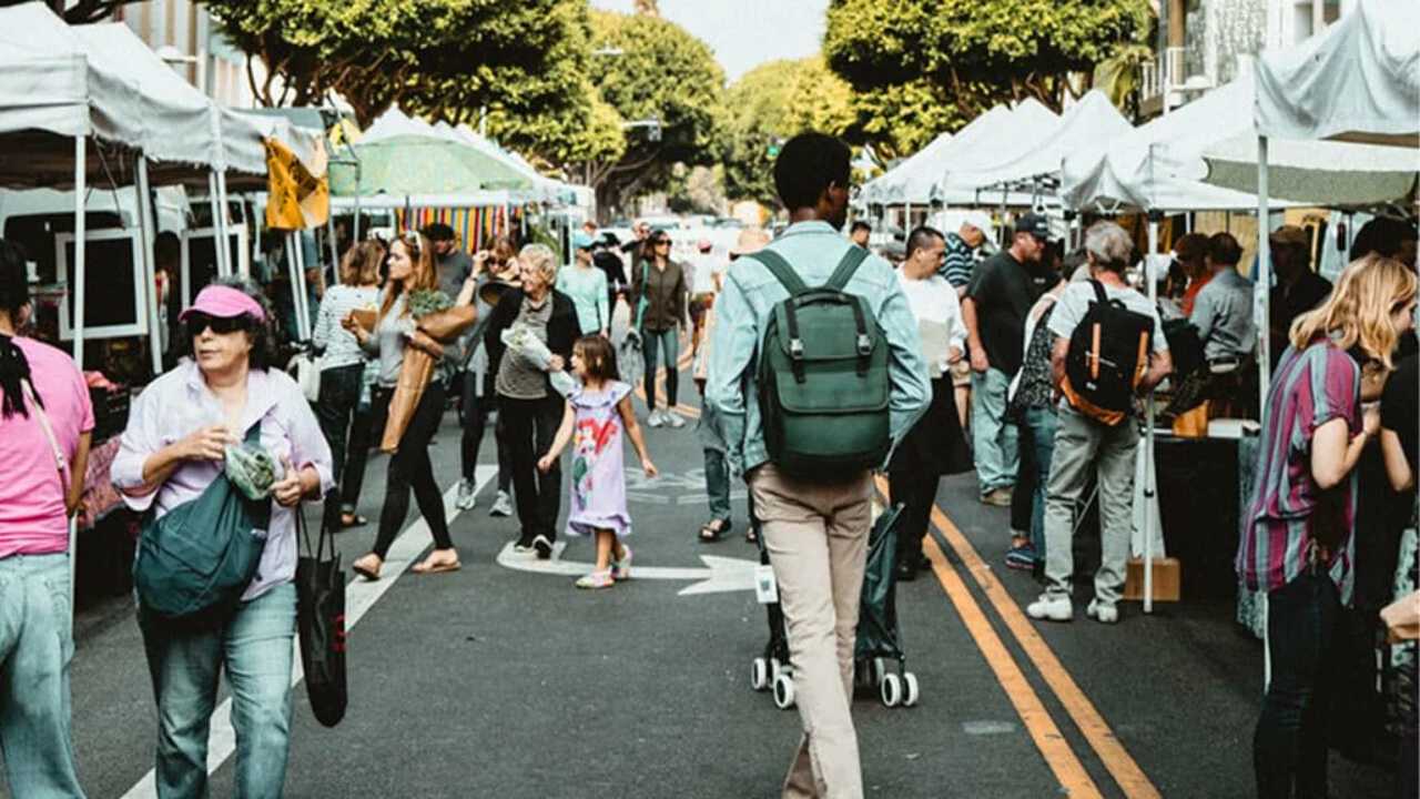 Eine Straßenpromenade, auf der viele Stände aufgebaut sind. Zwischen den Ständen laufen jede Menge Menschen hin und her.