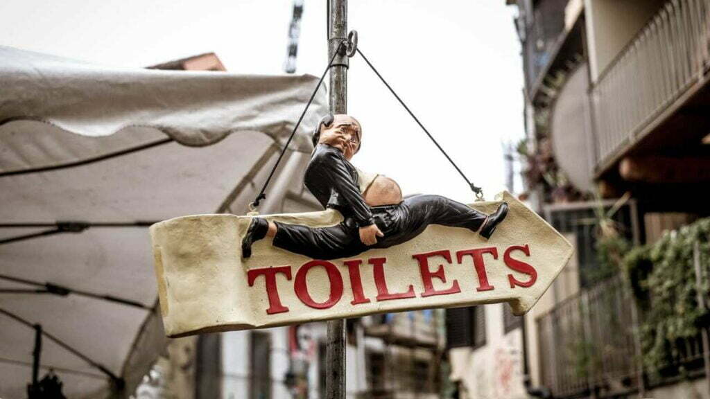 Ein Schild, auf dem "Toilets" geschrieben ist. Es zeigt nach rechts. Darüber befindet sich die Figur eines Mannes, der schnell rennt und sich dabei den Hintern hält.