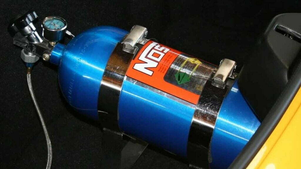 Eine blaue Flasche Lachgas. Diese ist mit zwei Metallgurten befestigt und hat auf dem Ablassventil einen Druckmesser montiert.