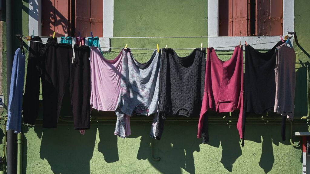 Eine lange Wäscheleine, auf der verschiedene Kleidungsstücke hängen. Dahinter befindet sich eine grüne Wand. Das Bild ist als visueller Gag zum Wort "Greenwashing" verwendet worden.
