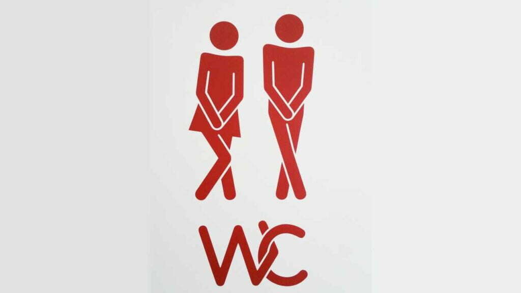 Zwei Strichfiguren, die sich die Hände vor den Schritt halten. Darunter steht "WC" mit verwobenen Buchstaben.