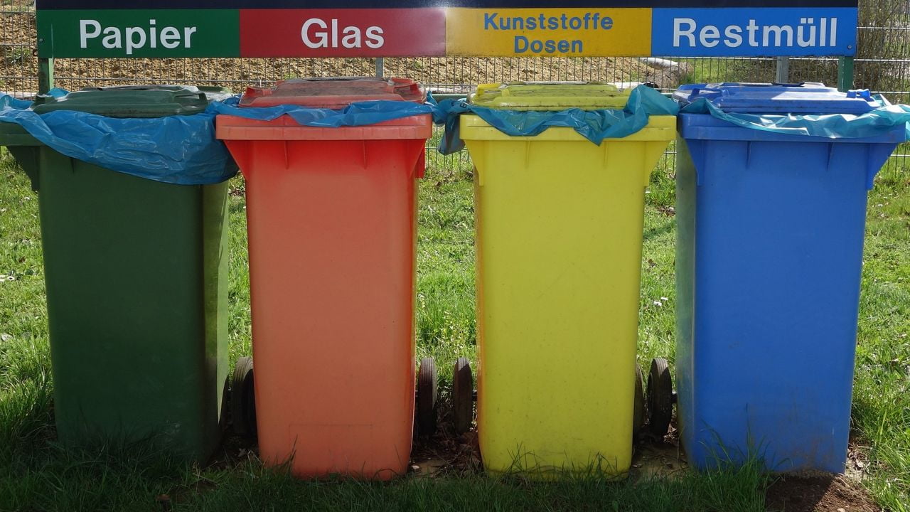 Vier Mülltonnen nebeneinander. Sie sind grün, rot, gelb und blau, mit den Beschriftungen Papier, Glas, Kunststoffe/Dosen und Restmüll.