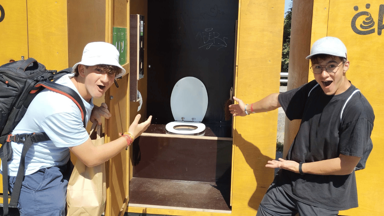 Zwei junge Männer zeigen lachend auf eine geöffnete ökologische Komposttoilette von öKlo auf einem Festival.